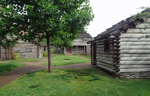 A row of log cabins in Fort Nashborough, a grassy area.