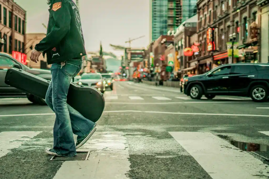 Musician with guitar crossing a Nashville street, showcasing a glimpse of Music City’s vibrant atmosphere